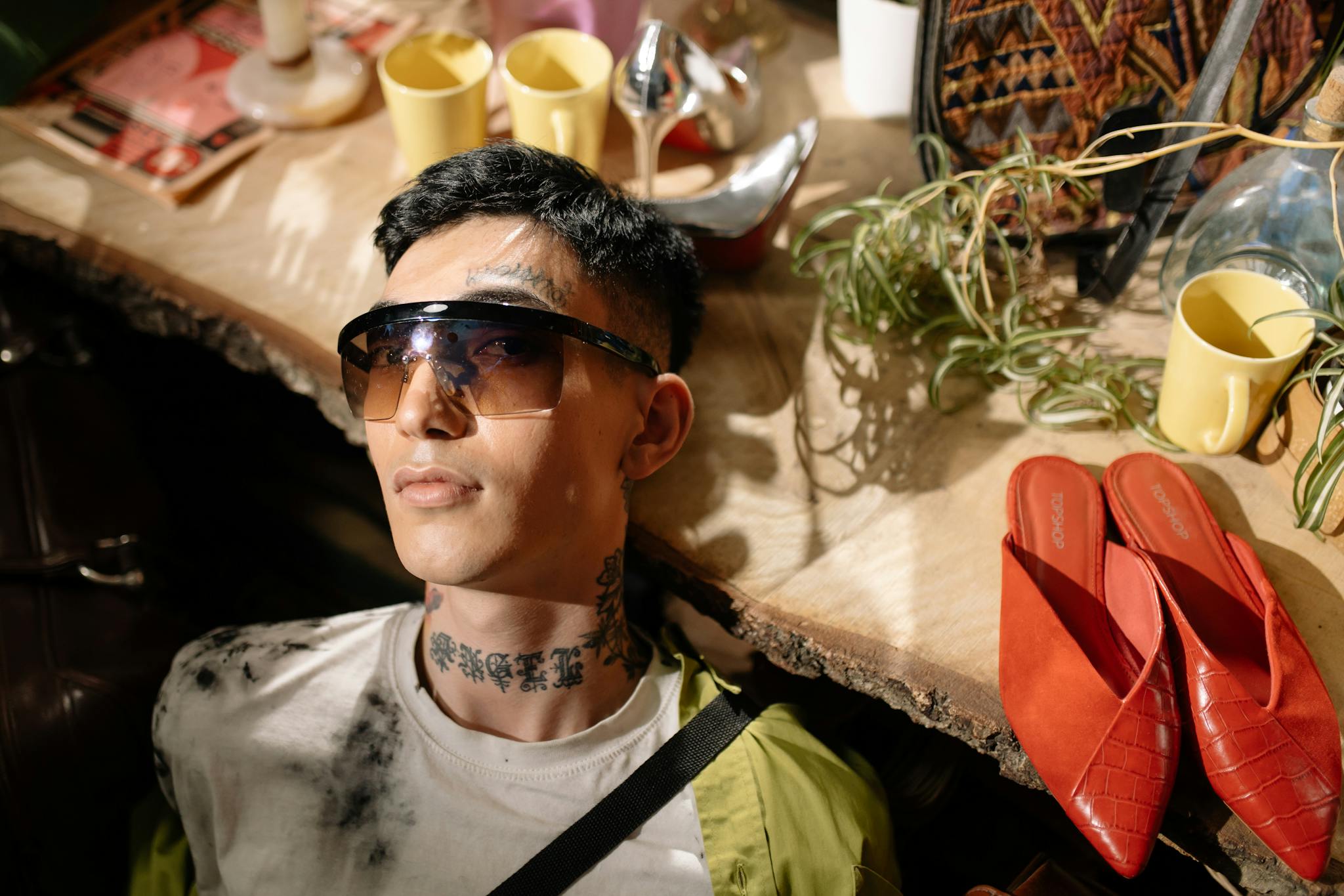 Portrait of a tattooed man in sunglasses surrounded by vintage accessories indoors.