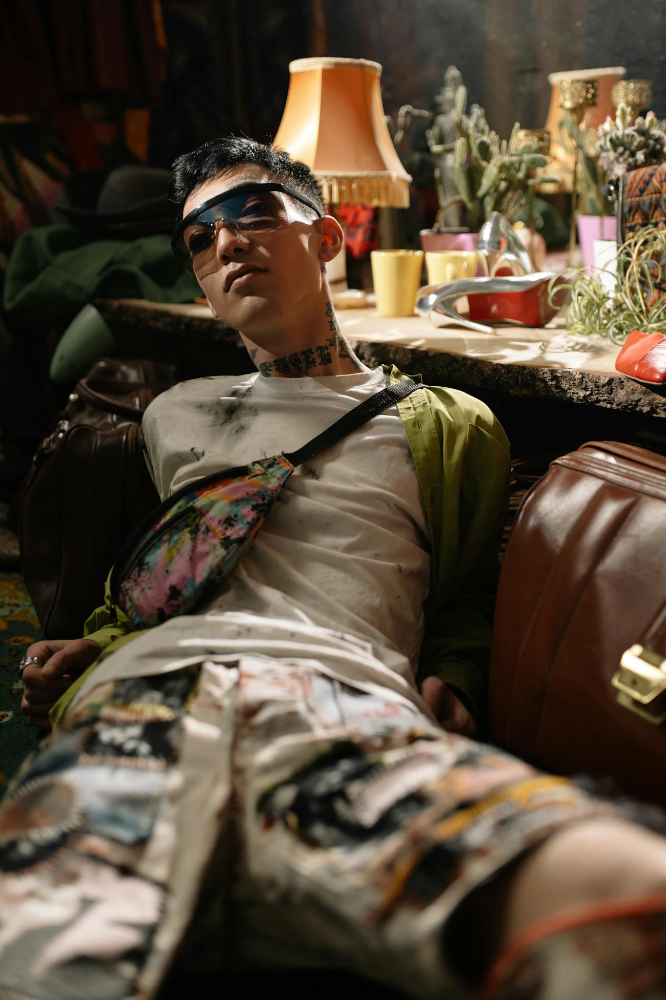 Stylish adult man in casual attire and sunglasses, relaxing indoors in a vibrant, eclectic room.